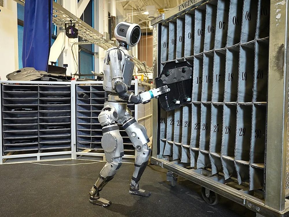 Atlas reaching into a rack carousel in a dim warehouse